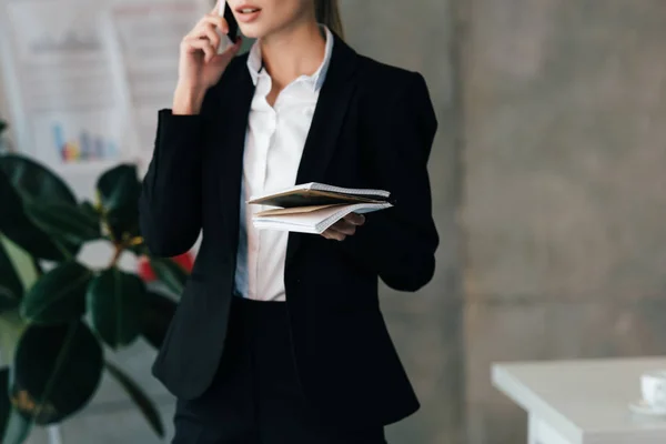 Cropped view of businesswoman talking on smartphone and holding documents — Stock Photo