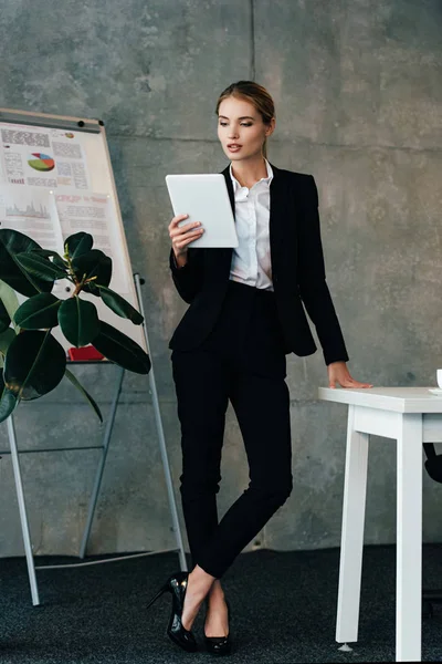 Attractive young businesswoman using digital tablet while standing by work desk in office — Stock Photo