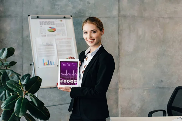 Smiling businesswoman showing digital tablet with heartbeat rate on screen — Stock Photo