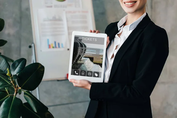 Vue recadrée d'une femme d'affaires souriante tenant une tablette numérique avec des billets à l'écran — Photo de stock