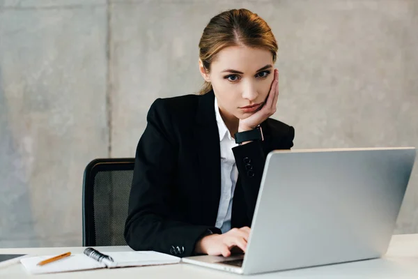 Femme d'affaires judicieusement concentrée utilisant un ordinateur portable et soutenant la tête avec la main — Photo de stock