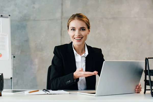 Felice donna d'affari sorridente che usa il computer portatile in ufficio e che punta lo schermo con mano — Foto stock