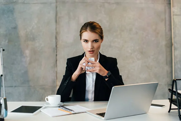 Pretty businesswoman sitting at workplace with crumpled paper in hands — Stock Photo