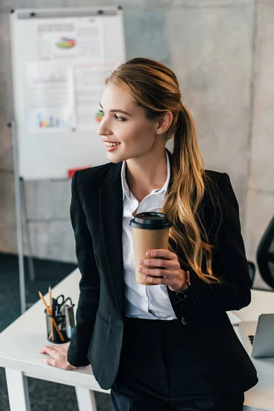 Foco seletivo de mulher de negócios sorridente ficar por mesa de trabalho com copo de descarte de café — Fotografia de Stock