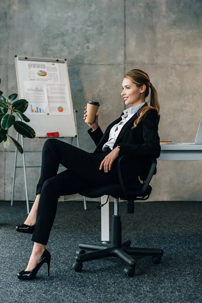 Mujer de negocios sonriente sentada en la silla con taza de papel de café — Stock Photo