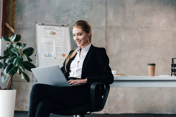 Smiling pretty businesswoman sitting on chair and using laptop — Stock Photo