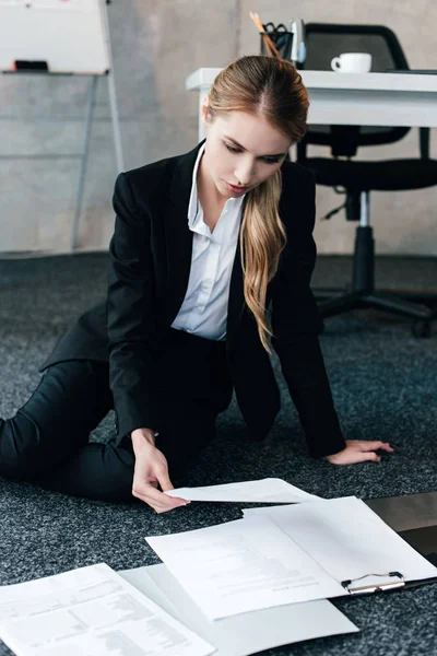 Bela mulher de negócios sentado no chão perto de mesa de trabalho e documentos de leitura — Fotografia de Stock