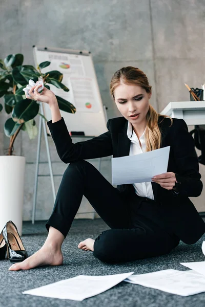 Schockierte Geschäftsfrau liest Dokument und sitzt barfuß auf dem Boden — Stockfoto
