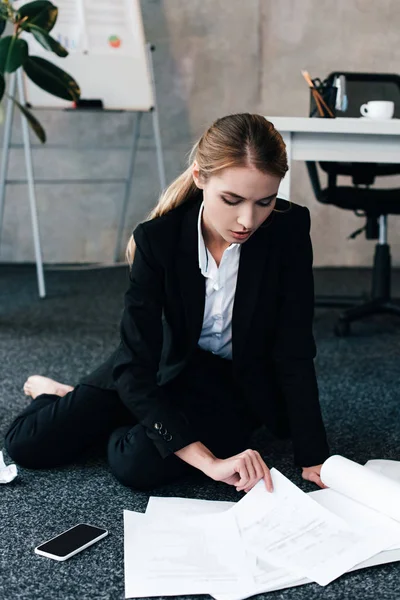 Mulher de negócios descalça sentado no chão perto de mesa de trabalho e documentos de leitura — Fotografia de Stock