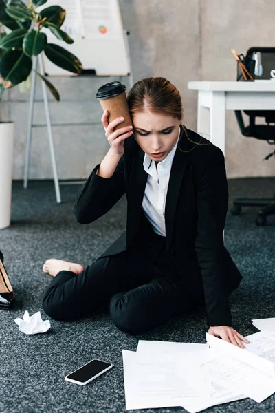 Exhausted businesswoman sitting on floor near work-table with headache — Stock Photo