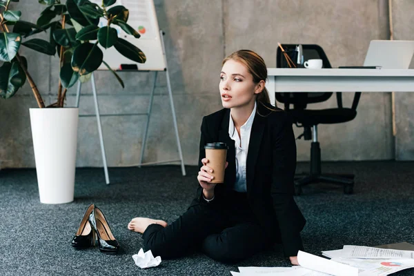 Hermosa mujer de negocios sentada en el piso cerca de la mesa de trabajo y la celebración de café - foto de stock