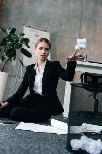 Businesswoman sitting on floor and throwing napkin to basket — Stock Photo