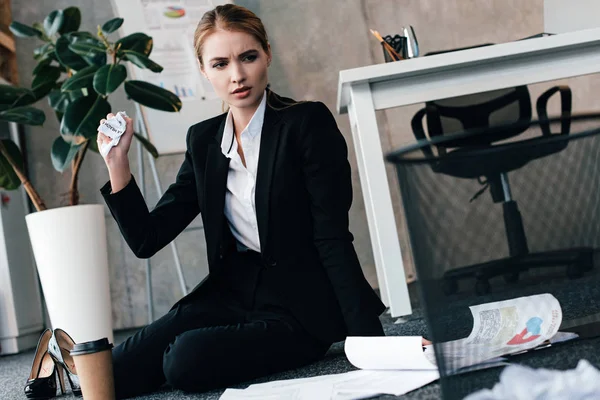 Вдумлива бізнес-леді, що сидить на підлозі біля робочого столу з кавою та документами — стокове фото