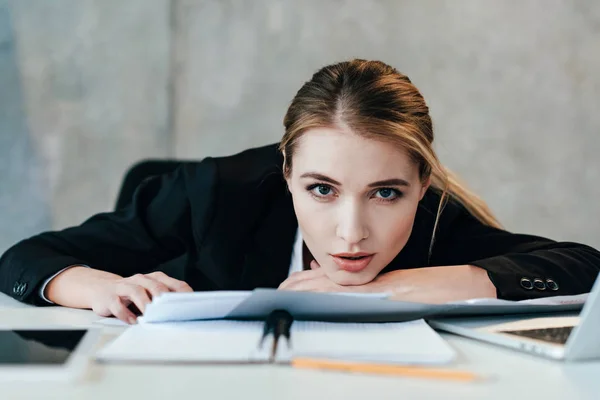 Selective focus of businesswoman looking at camera and sitting at work-table with documents — Stock Photo