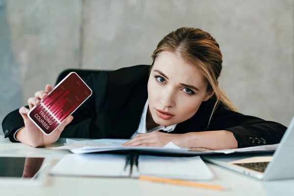 Selective focus of businesswoman at work-table showing screen of smartphone with trading courses — Stock Photo