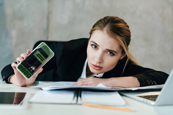 Selektive Fokussierung der Geschäftsfrau am Arbeitsplatz zeigt Bildschirm des Smartphones mit Buchungs-App — Stockfoto