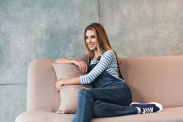 Joven hermosa mujer sonriendo, abrazando almohada y sentado en sofá rosa - foto de stock