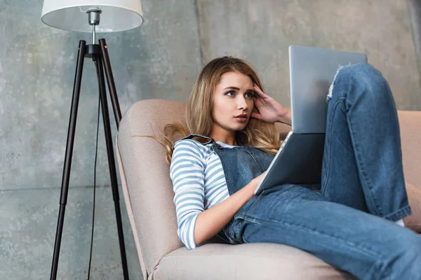 Shocked adult woman thinking and looking at monitor of laptop — Stock Photo