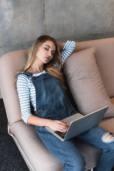 Young beautiful girl dreaming on pink sofa with laptop — Stock Photo