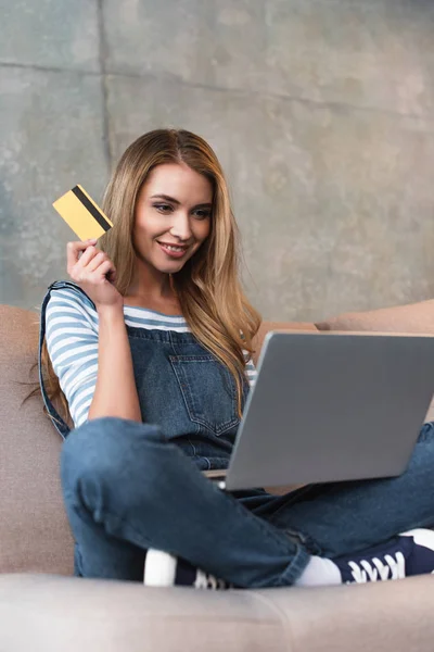Красива жінка Холдинг кредитної картки, сидячи на дивані з ноутбуком — стокове фото