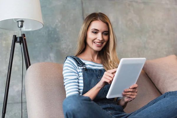 Junge Frau sitzt auf rosa Sofa und nutzt digitales Tablet — Stockfoto