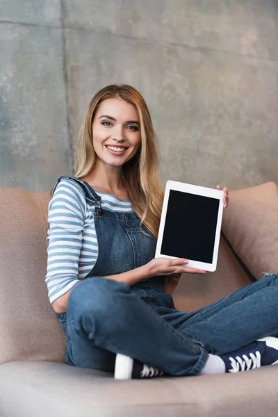 Jovem sentada no sofá e mostrando tela em branco do tablet digital — Fotografia de Stock