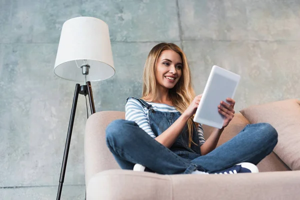 Glückliches junges Mädchen lächelt und nutzt digitales Tablet im Zimmer — Stockfoto