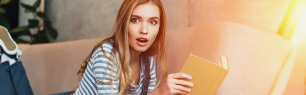 Schockierte junge Frau im Zimmer mit Sonnenschein und Buch in der Hand — Stockfoto