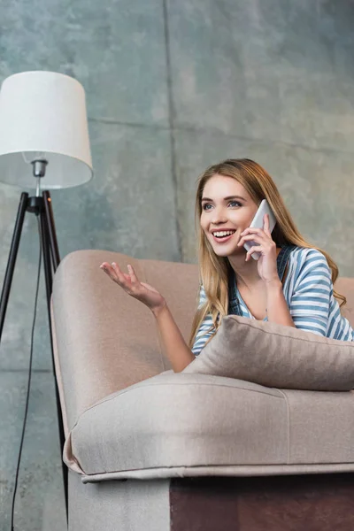 Happy woman talking on smartphone and lying on pink sofa — Stock Photo