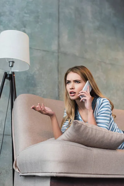 Worried woman talking on smartphone and lying on pink sofa — Stock Photo