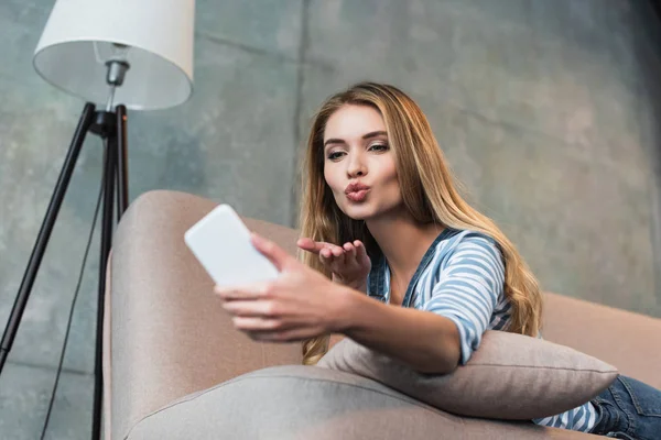 Chica adulta acostada en un sofá rosa y tomando selfie en el teléfono inteligente - foto de stock