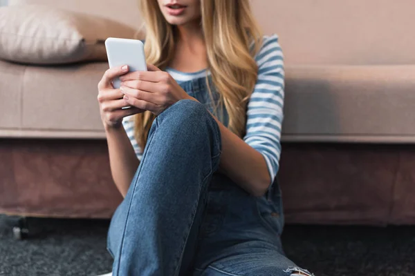 Обрезанный вид молодой женщины с помощью смартфона и сидя рядом с розовым диваном — стоковое фото