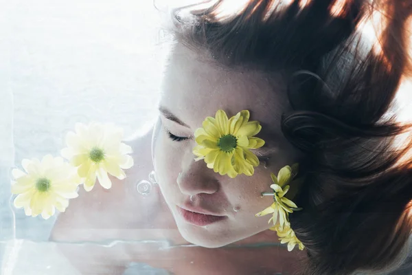 Nahaufnahme eines jungen Mädchens, das unter Wasser mit Blumen posiert — Stockfoto