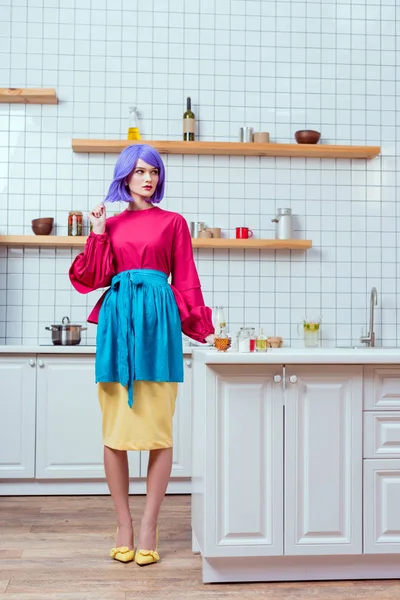 Belle femme au foyer avec des cheveux violets et des vêtements colorés posant dans la cuisine avec espace de copie — Photo de stock