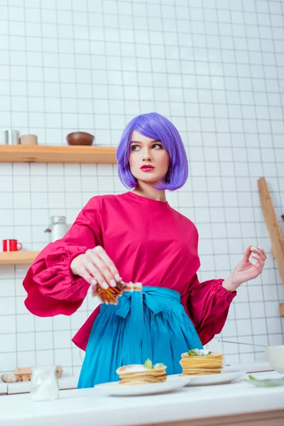 Selektiver Fokus der Hausfrau mit lila Haaren und bunten Kleidern, die in der Küche Sirup auf Pfannkuchen gießt — Stockfoto