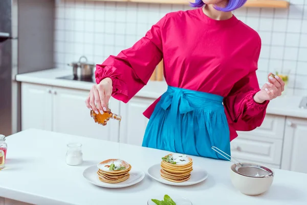 Vista cortada de dona de casa em roupas coloridas derramando xarope em panquecas na cozinha — Fotografia de Stock