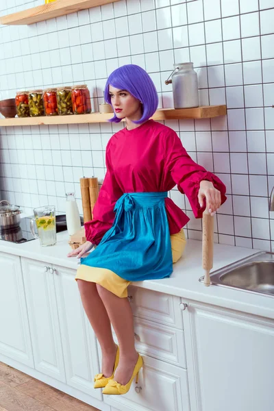 Foyer sélectif de la femme au foyer avec les cheveux violets assis sur le comptoir de cuisine avec rouleau à pâtisserie — Photo de stock