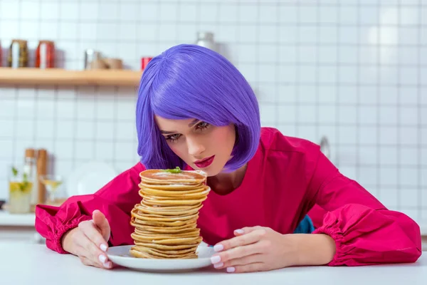 Bela dona de casa com cabelo roxo olhando para a placa com panquecas na cozinha — Fotografia de Stock