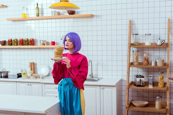 Foco seletivo de bela dona de casa com cabelo roxo segurando placa com panquecas na cozinha — Fotografia de Stock