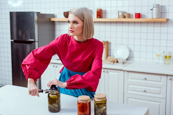 Beautiful stylish housewife sealing jar of pickled cucumbers in kitchen — Stock Photo