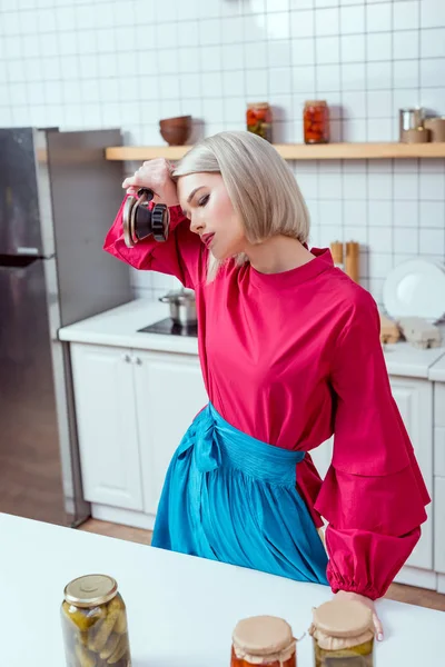 Beautiful tired housewife with can sealing machine and jars of pickled vegetables in kitchen — Stock Photo