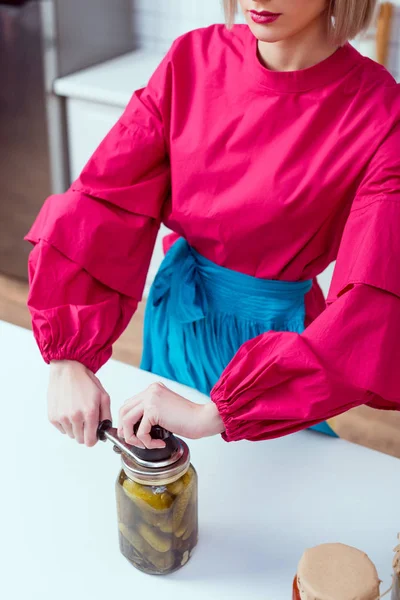 Cropped view of fashionable housewife sealing jar of pickled cucumbers in kitchen — Stock Photo