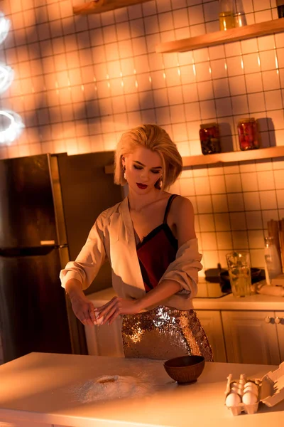 Hermosa ama de casa con harina en el mostrador de cocina en la cocina con luz naranja - foto de stock