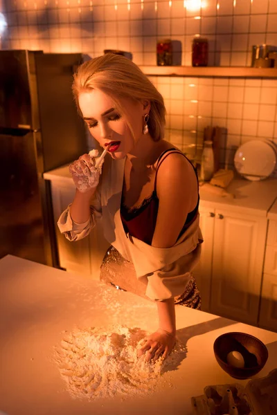 Beautiful elegant housewife smoking cigarette while cooking in kitchen with orange light — Stock Photo