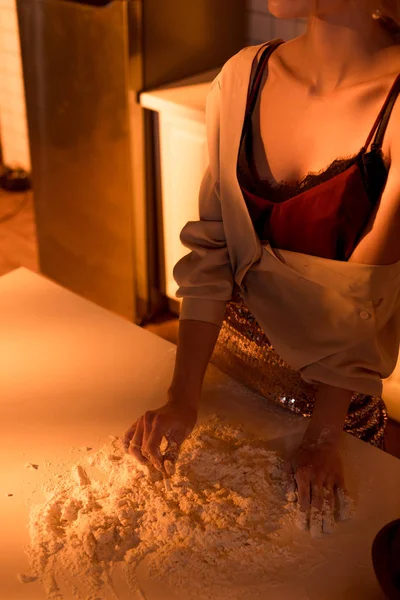 Vista cortada da mulher colocando fora o cigarro na farinha ao cozinhar na cozinha com luz laranja — Fotografia de Stock