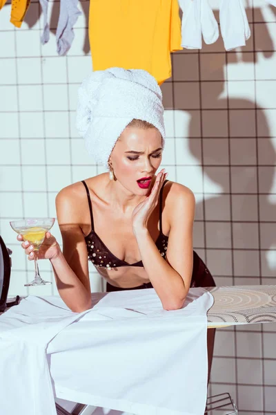 Hermosa impactada ama de casa en la toalla celebración de copa de cóctel en el baño - foto de stock
