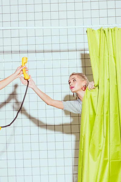 Hermosa mujer tomando teléfono retro amarillo auricular en la ducha con cortina verde - foto de stock