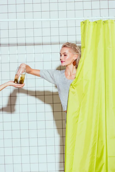 Beautiful woman taking pickled cucumber from glass jar in shower — Stock Photo