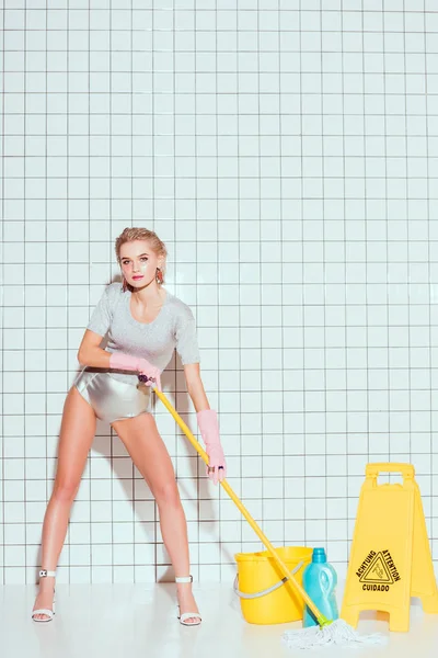 Belle femme au foyer regardant la caméra tout en nettoyant le sol dans la salle de bain — Photo de stock