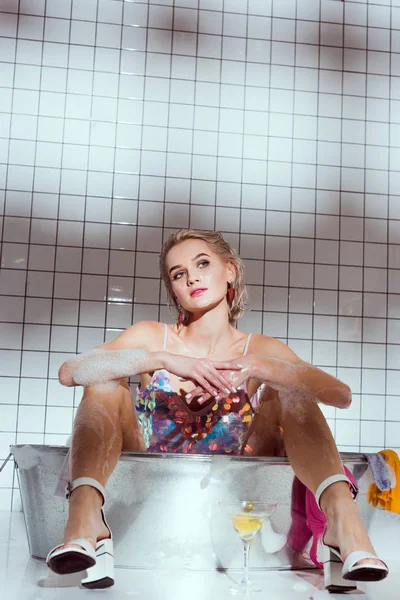 Mujer joven con estilo sentado en la bañera de lavado y mirando hacia otro lado - foto de stock